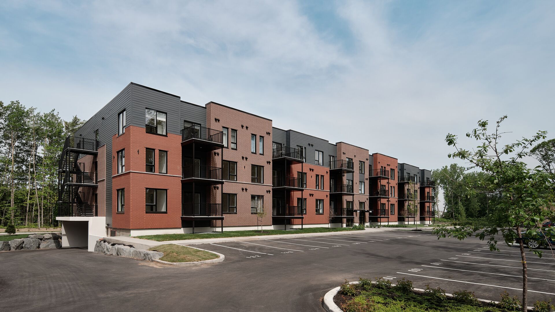 Façade du William Henry, un immeuble de condos locatifs de trois étages en brique et revêtement gris, avec balcons et stationnement extérieur, à Sorel-Tracy.
